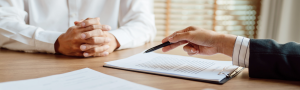 hand with pen getting ready to sign a document with another person at the table